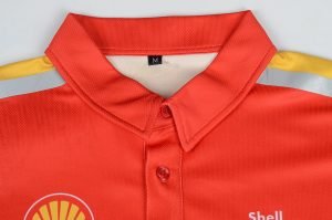 Shell branded red and yellow work uniform polo shirt with reflective strips and a button-up collar, designed for industrial or safety work environments.