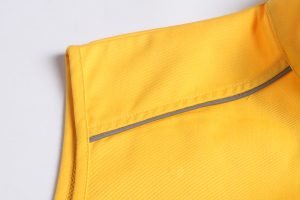 Bright yellow workwear uniform fabric close-up with reinforced stitching and reflective strip for safety in industrial environments.
