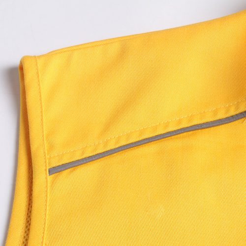 Bright yellow workwear uniform fabric close-up with reinforced stitching and reflective strip for safety in industrial environments.