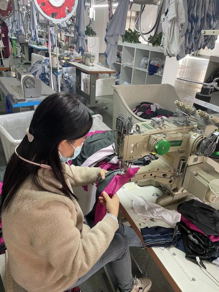 High-quality industrial sewing machine producing custom uniforms in a factory setting with fabric, textiles, and garment pieces.