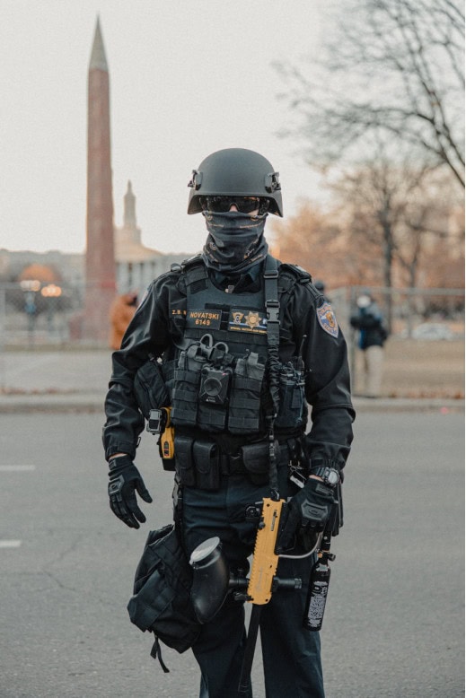 Military police officer in tactical gear and body armor during an outdoor event in an urban area.