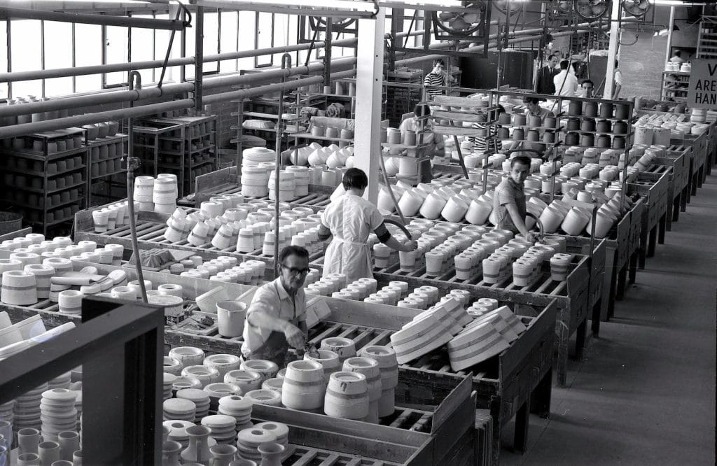 Uniform manufacturing factory with workers assembling ceramic or plastic ware for industrial use.