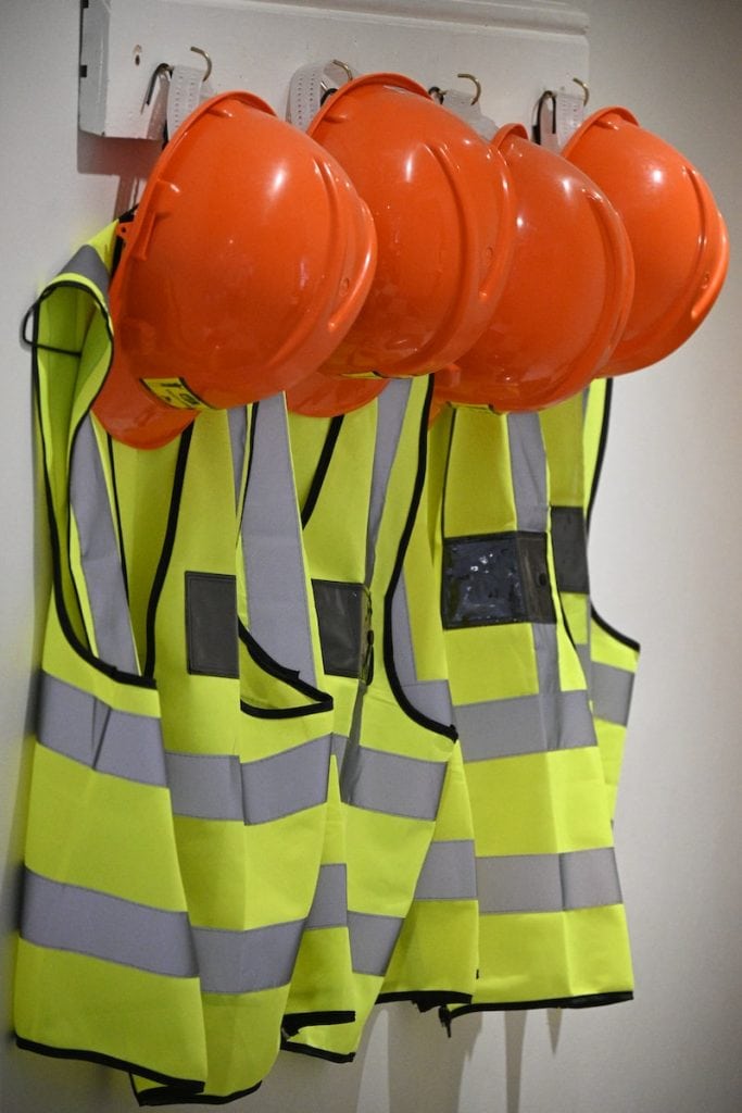 High-visibility safety vests and orange construction helmets hanging on a wall display, essential workwear for safety and protection in construction and industrial environments.