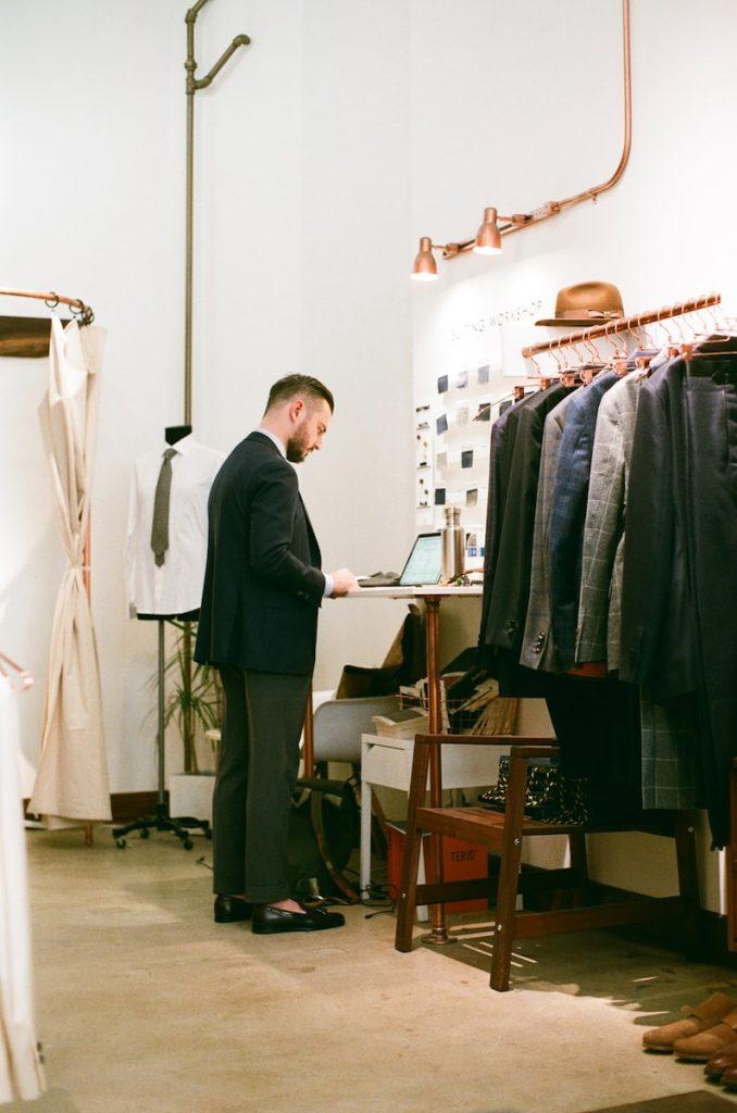Men adjusting custom-designed work uniforms in a clothing showroom with tailored suits and accessories.