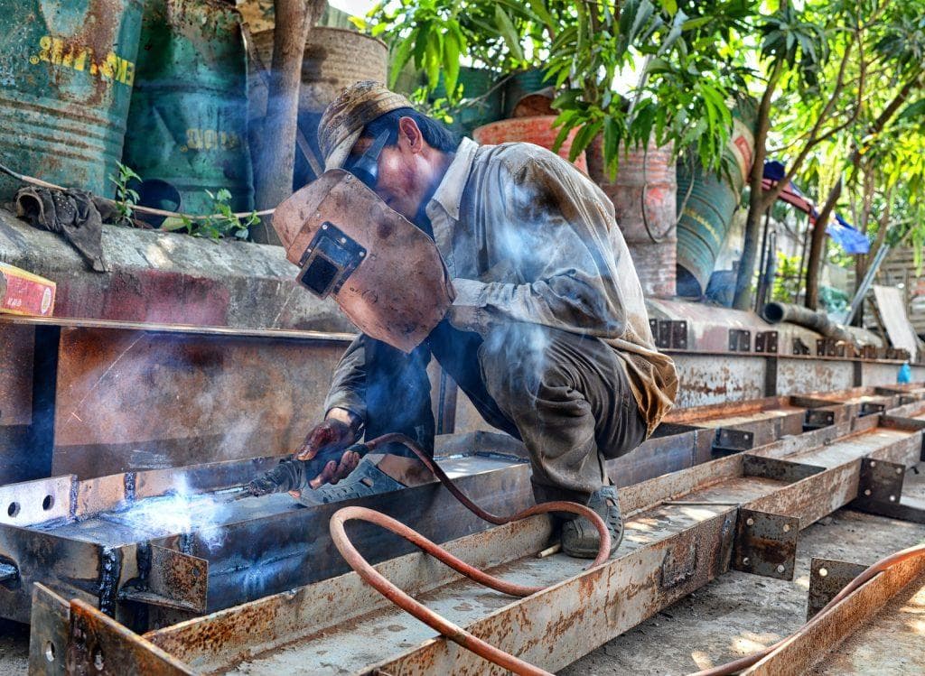 Welding worker in protective gear welding metal framework outdoors at a construction site.