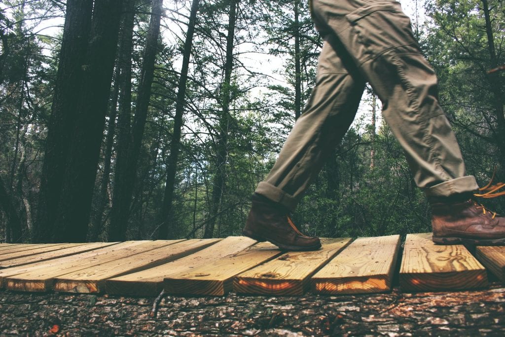 Wearing work boots and khaki work pants while walking on a wooden path in the forest.