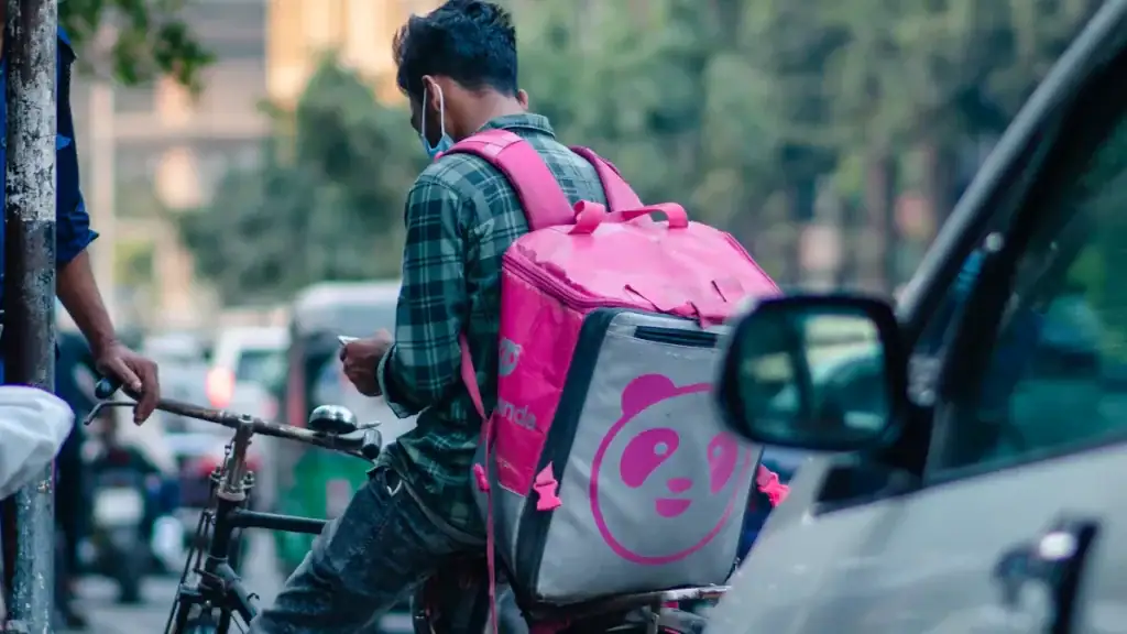 Pink and gray panda-themed insulated delivery bag carried on a cyclist's back on a city street.