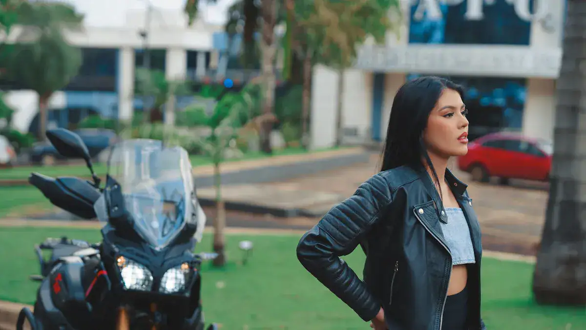 Stylish woman in a black leather jacket standing outdoors with a motorcycle in the background.