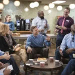 Comfortable workplace meeting with diverse team members wearing custom uniforms in a modern coffee shop, engaging in a lively discussion.