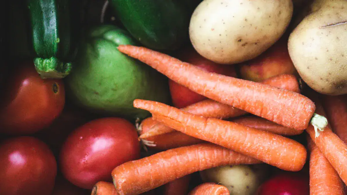 Fresh organic carrots, potatoes, green bell pepper, and tomatoes on a market shelf.