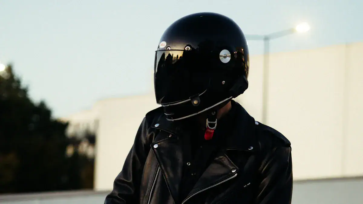 Rider wearing a black leather jacket and a full-face black helmet, standing outdoors at dusk.