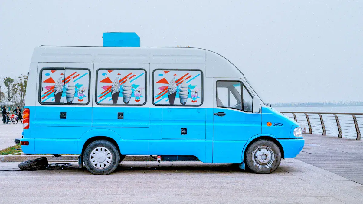Bright blue ice cream truck with colorful ice cream and cartoon characters on the windows, parked by the waterfront on a cloudy day.