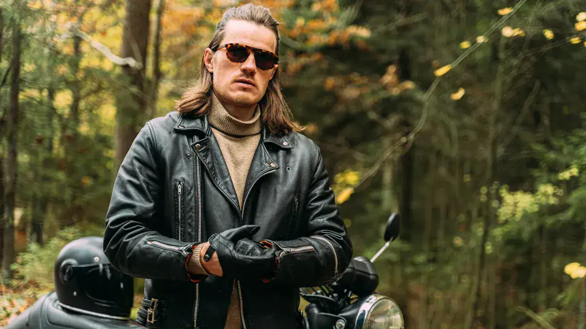 Rugged man wearing leather jacket and sunglasses in forest setting, outdoor motorcycle rider style, autumn foliage in background.