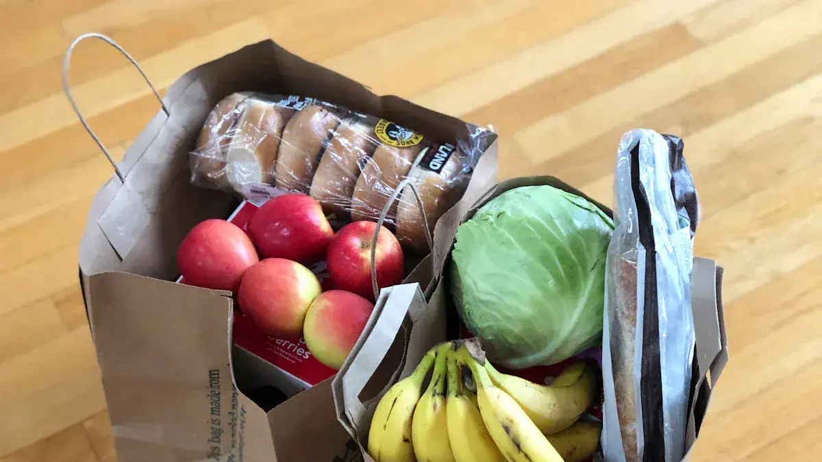 Fresh apples, bananas, lettuce, and packaged bread in a brown paper grocery bag on a wooden floor.