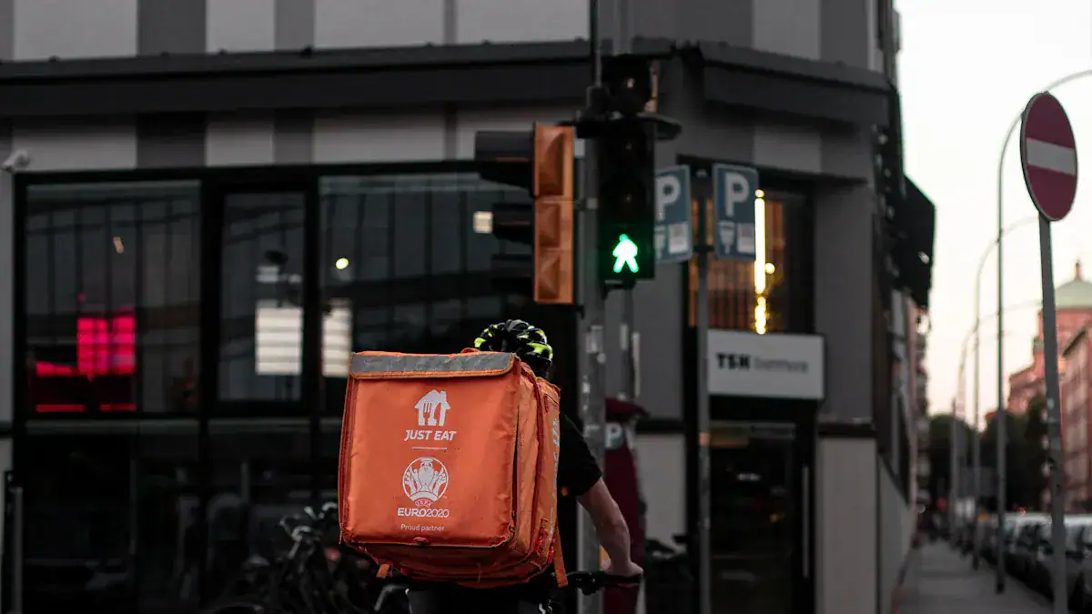 Orange delivery backpack for food courier with Euro 2020 logo and "Just Eat" branding on city street, showing urban logistics and branded uniforms.