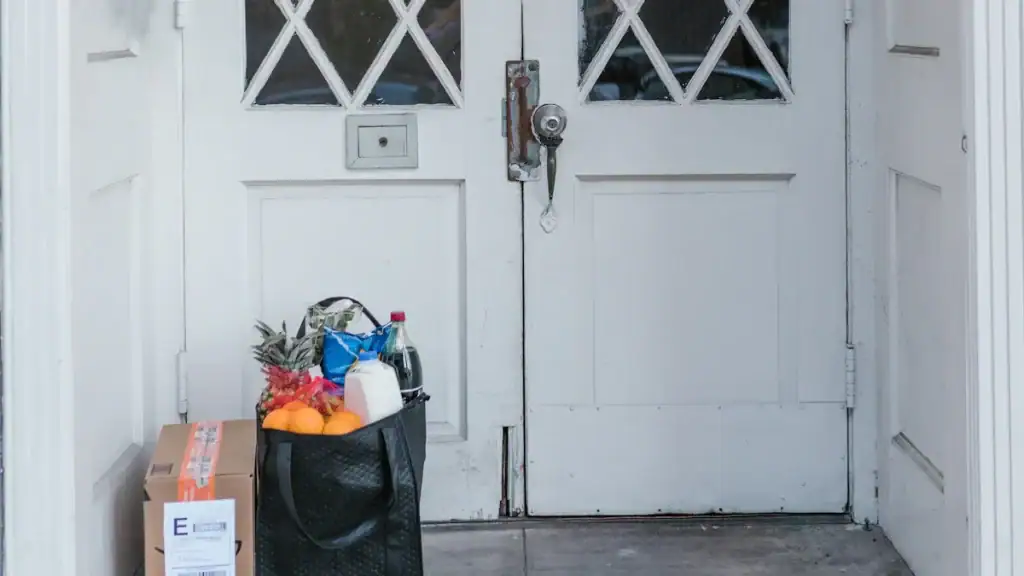 Pineapple, orange, milk, and grocery items in a black shopping bag in front of a white door with a padlock.