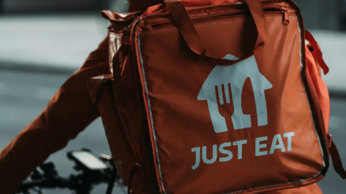 Bright orange delivery backpack with "Just Eat" logo, designed for food delivery services, featuring a spacious compartment and sturdy straps for secure transportation.