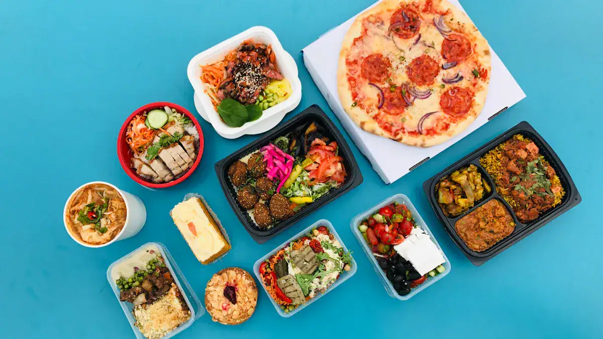 Assorted takeout dishes including pizza, salads, rice bowls, and desserts displayed on a blue surface.