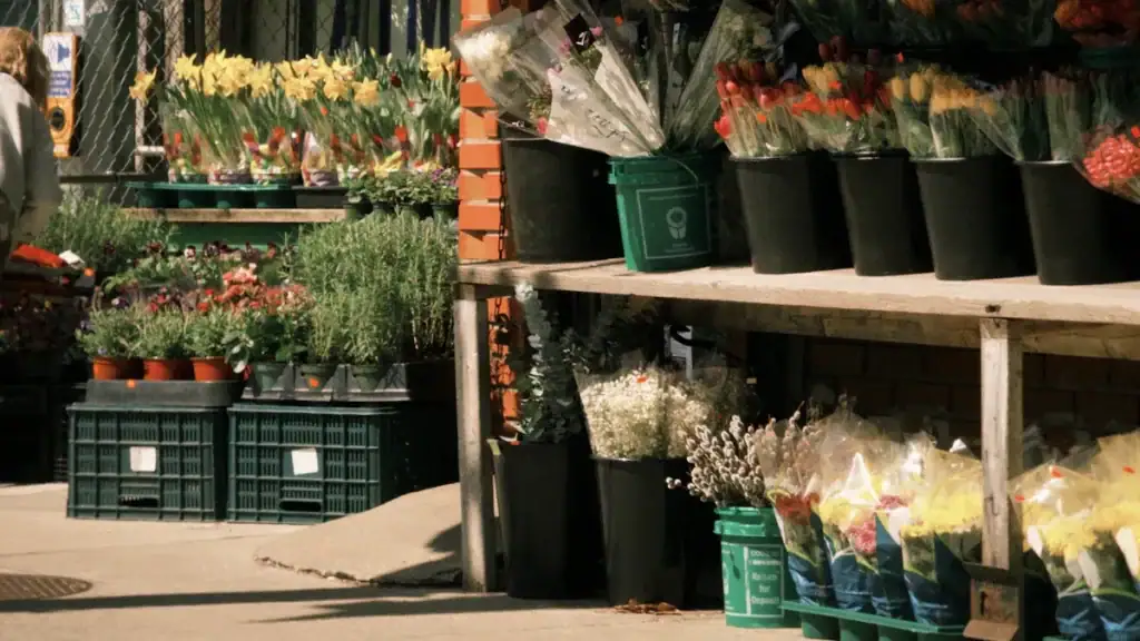 Flower shop with potted flowers and bouquets displayed outside, bright colorful blooms in black pots and plastic buckets on outdoor shelves, vibrant floral arrangements for sale in a garden center or flower market.