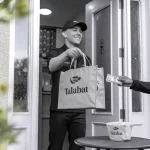 Freshly delivered Talabat food order being handed over at the doorstep with delivery staff wearing customized uniforms. The image highlights professional clothing for food delivery services.