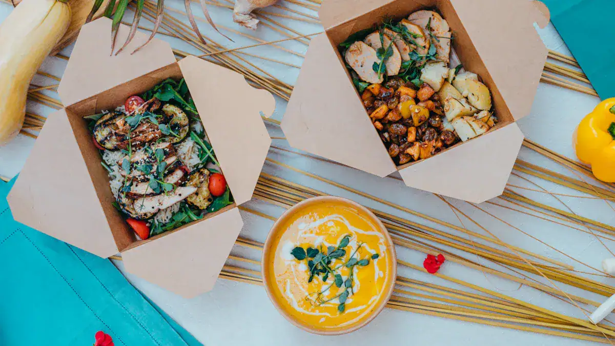 Fresh Asian-style takeout containers with colorful vegetable and chicken dishes, served with a bowl of bright yellow soup, laid out on a decorative mat with scattered herbs and vegetables, ideal for food delivery or catering.
