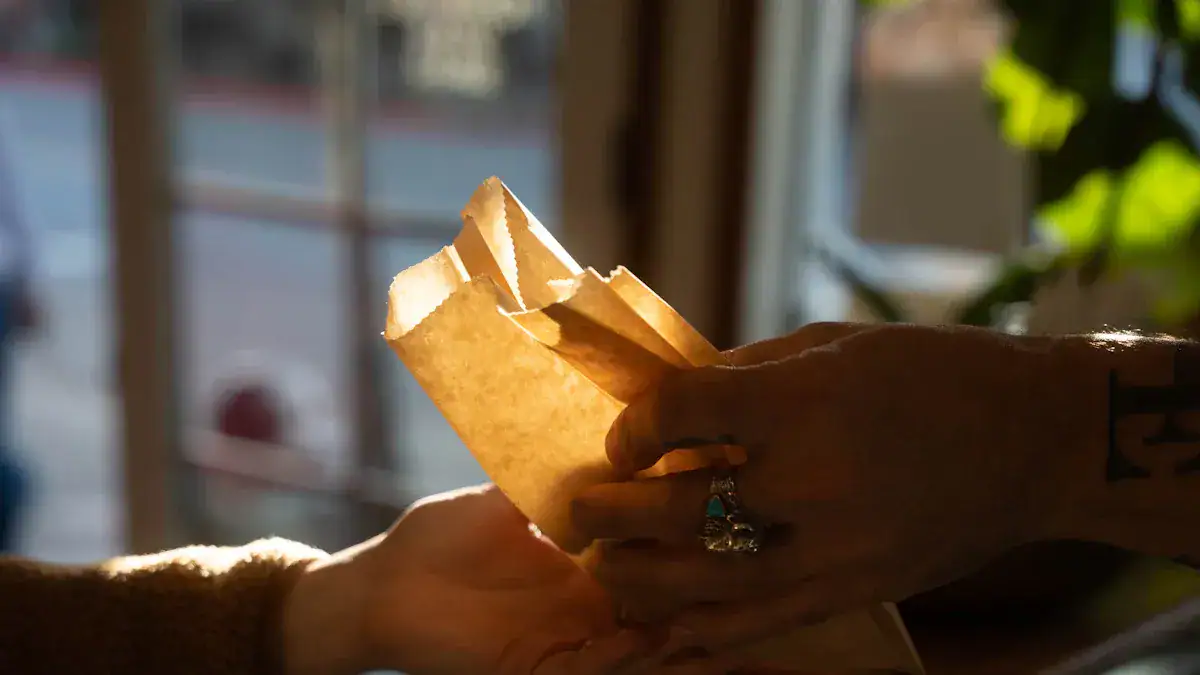 Hand holding a paper bag delivering food at a restaurant or café.