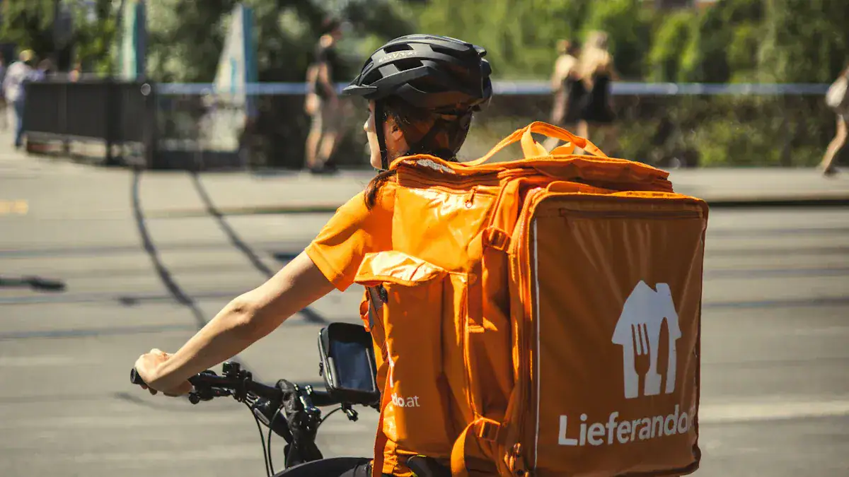 Delivery courier in bright orange uniform riding a bicycle with a large insulated delivery backpack on the back, outdoors, city street background, efficient food delivery service.