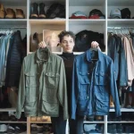 Versatile worker holding up two different work jackets in a spacious closet filled with uniforms, shoes, and accessories, showcasing custom workwear options from a China-based manufacturer.