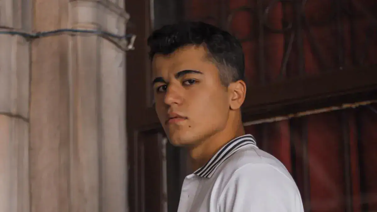 Young man wearing a white casual shirt with a striped collar, standing near a rustic barn door.