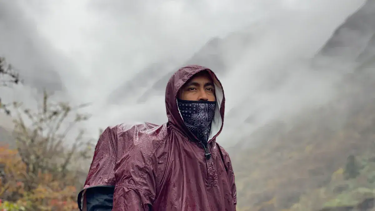 Waterproof maroon outdoor rain jacket worn by a man in a misty mountain landscape.