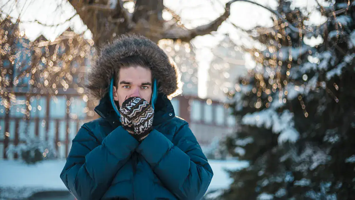 Warm winter clothing for men, young man in a blue insulated jacket and patterned gloves, standing outdoors in snowy winter landscape.