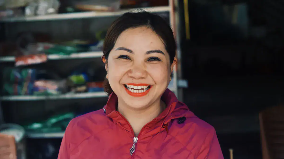 Bright smiling woman in red workwear jacket, smiling at the camera in a workshop or store setting.