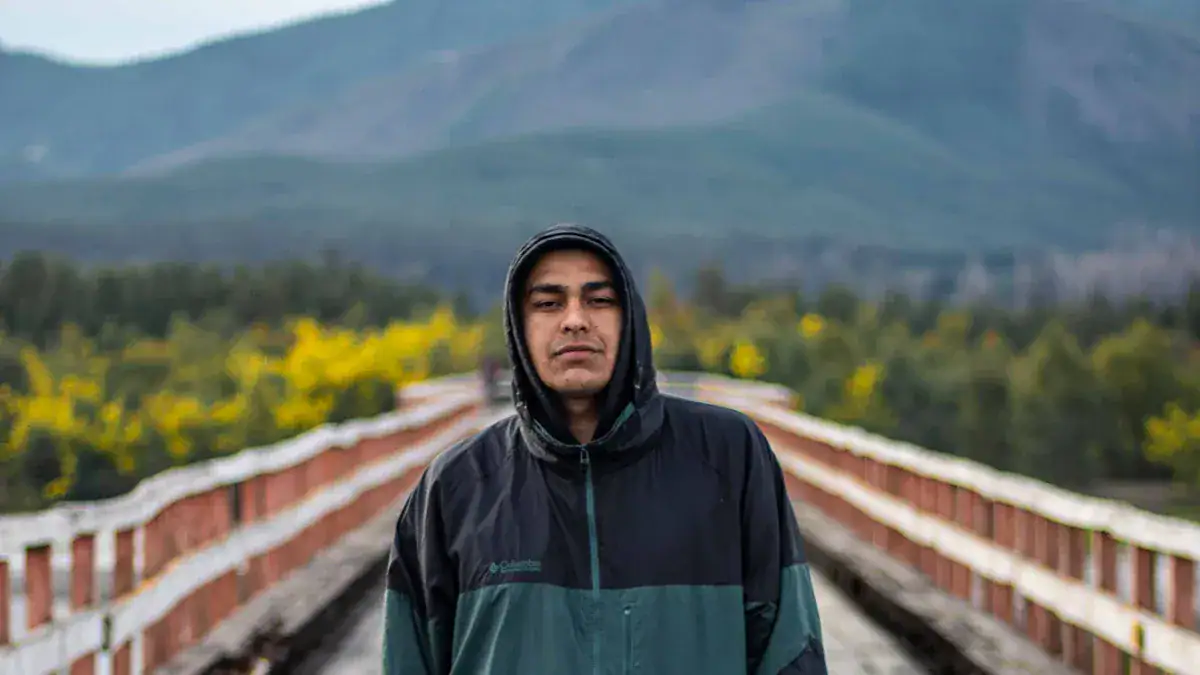High-quality waterproof outdoor jacket worn by a man standing on a scenic bridge with mountains in the background, showcasing durable custom workwear clothing from a Chinese manufacturer.