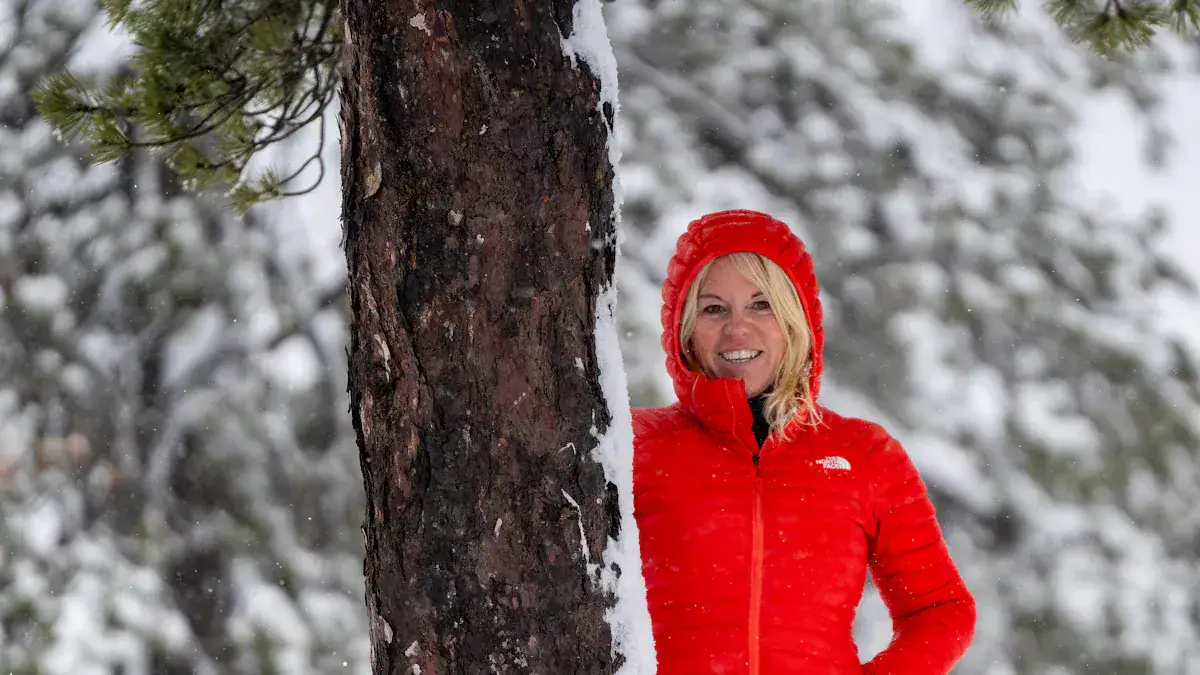 Warm red winter jacket with hood on smiling woman in snowy forest scene.