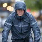 Waterproof raincoat jacket worn by a cyclist in rainy weather for outdoor work or sports.