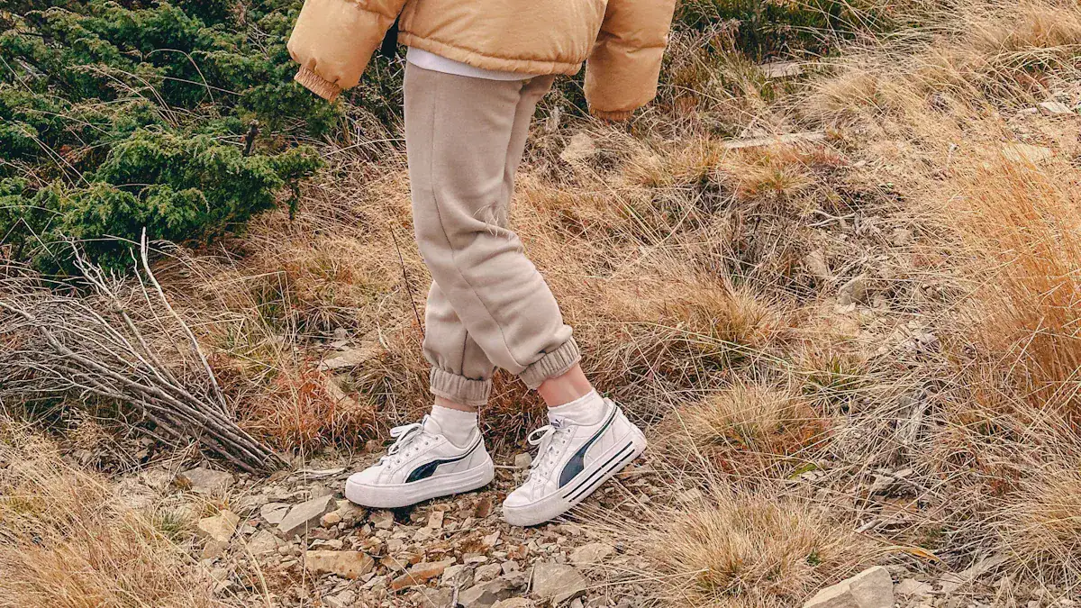 Comfy casual sneakers and joggers worn by a person outdoors on rocky terrain with dry grass and greenery.