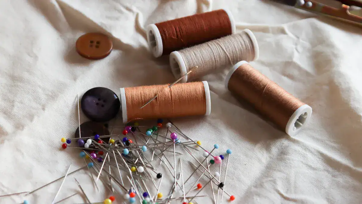 Spools of sewing thread, colorful sewing pins, and buttons on fabric, showcasing tailoring and custom clothing manufacturing in China.