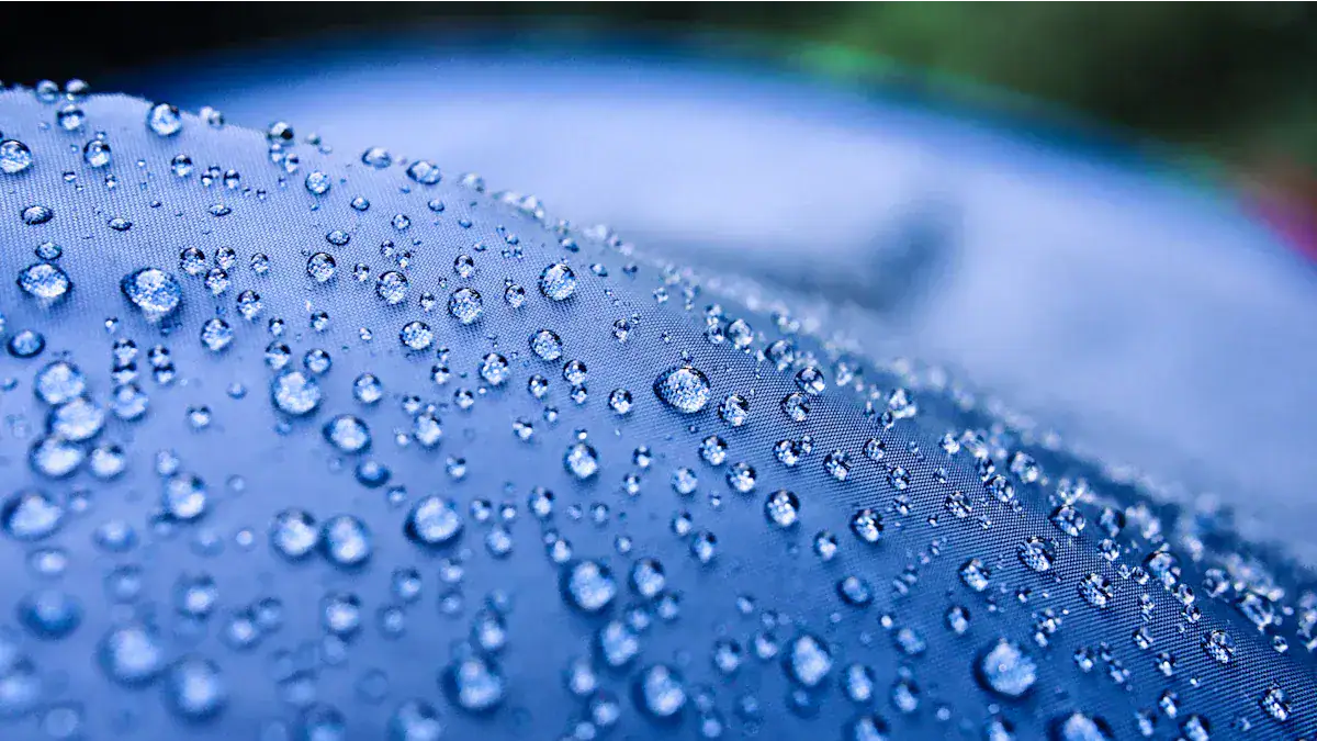 Water droplets on a blue waterproof fabric, highlighting the durable and high-quality material used in custom workwear and uniforms.