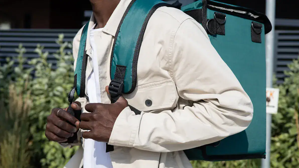 High-quality delivery person wearing a beige jacket and carrying a teal insulated delivery backpack for food or parcel transport on urban streets.