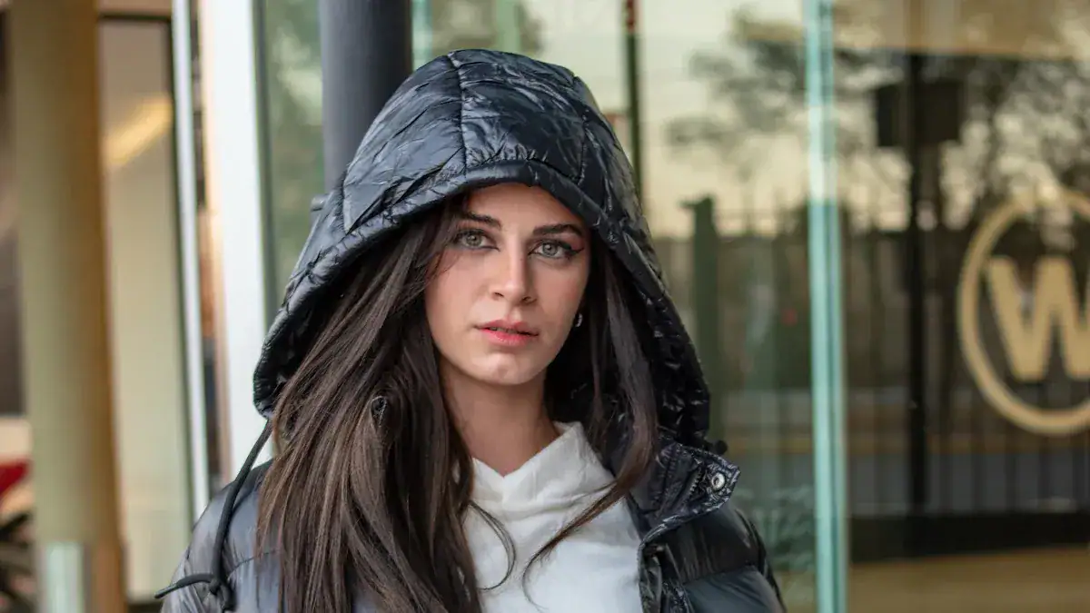 Stylish woman in black raincoat with hood, outdoor urban setting, fashionable weather-resistant clothing, modern casual apparel for rain protection.