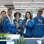 Bright team wearing custom branded uniforms shaking hands in modern office environment, showcasing corporate workwear solutions from China manufacturer.