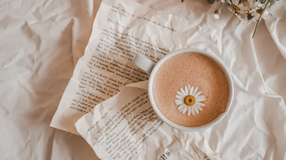 Cappuccino with a daisy flower floating on top, placed on crumpled newspaper and white fabric, creating a cozy and aesthetic morning scene.