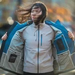 High-performance outdoor jacket worn by a woman in a windy outdoor setting, showcasing durable construction and weather-resistant fabric.