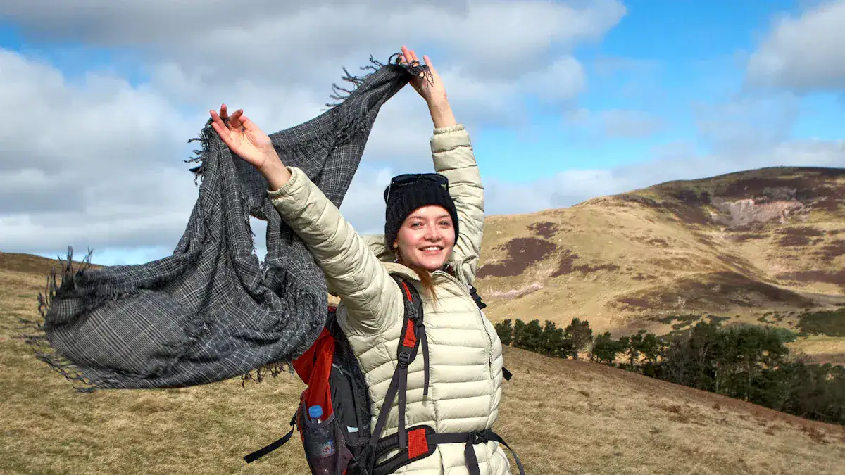 Warm outdoor jacket and hiking gear worn by a smiling woman enjoying nature on a mountain trail in daytime.