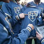 High-quality custom blue jackets with embroidered logos displayed on a tablet, worn by a group of people in a professional outdoor setting.