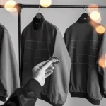 Custom black and gray work jackets with reinforced stitching, displayed on hangers in a manufacturing setting.