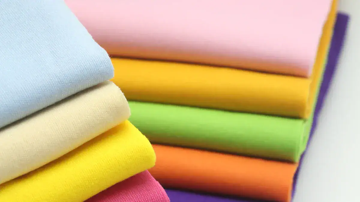 Vibrant stacked fabrics in various colors including blue, yellow, pink, green, and orange, showcasing high-quality textile materials for custom clothing and uniforms from a trusted Chinese manufacturer.