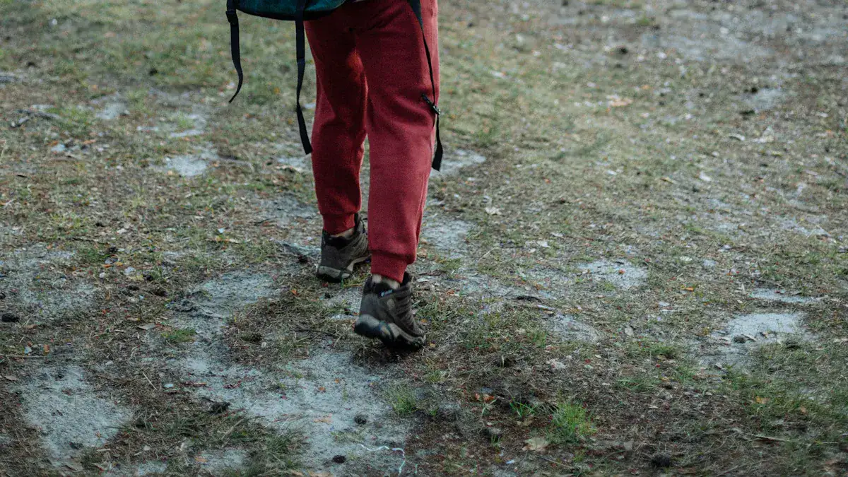 Comfortable hiking shoes and red trekking pants walking on muddy trail in outdoor terrain.