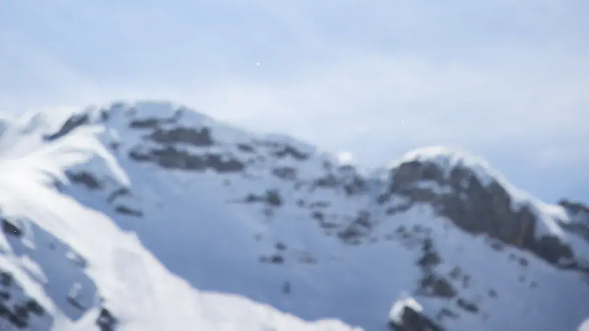 Blurry snowy mountain landscape with peaks and a blue sky, representing outdoor workwear and rugged apparel for challenging environments.