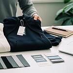 High-quality custom hoodies and sweatshirts with branded tags, fabric swatches, and color options displayed on a work table for clothing manufacturing.